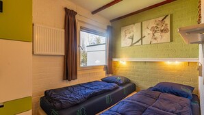 Una habitación con dos camas individuales, una ventana con cortinas, un radiador y una lámpara fijada a la pared.