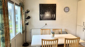 Et spiseområde med et hvidt bord, træstole, en sort pendel, et ur og et billede i ramme på væggen.