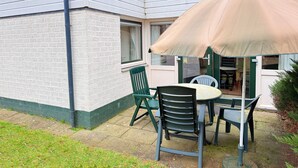 En terrasse med et bord og stole, en beige parasol og en murstensvæg.