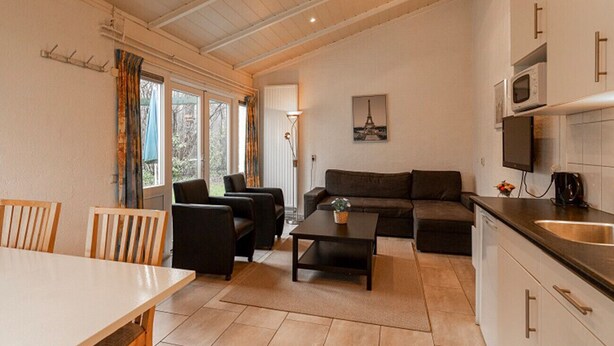 A modern living room with a sofa, coffee table, and dining area. There is a kitchen with a microwave and sink. - Bungalowpark Simpelveld - Schakel 5 (Simpelveld)