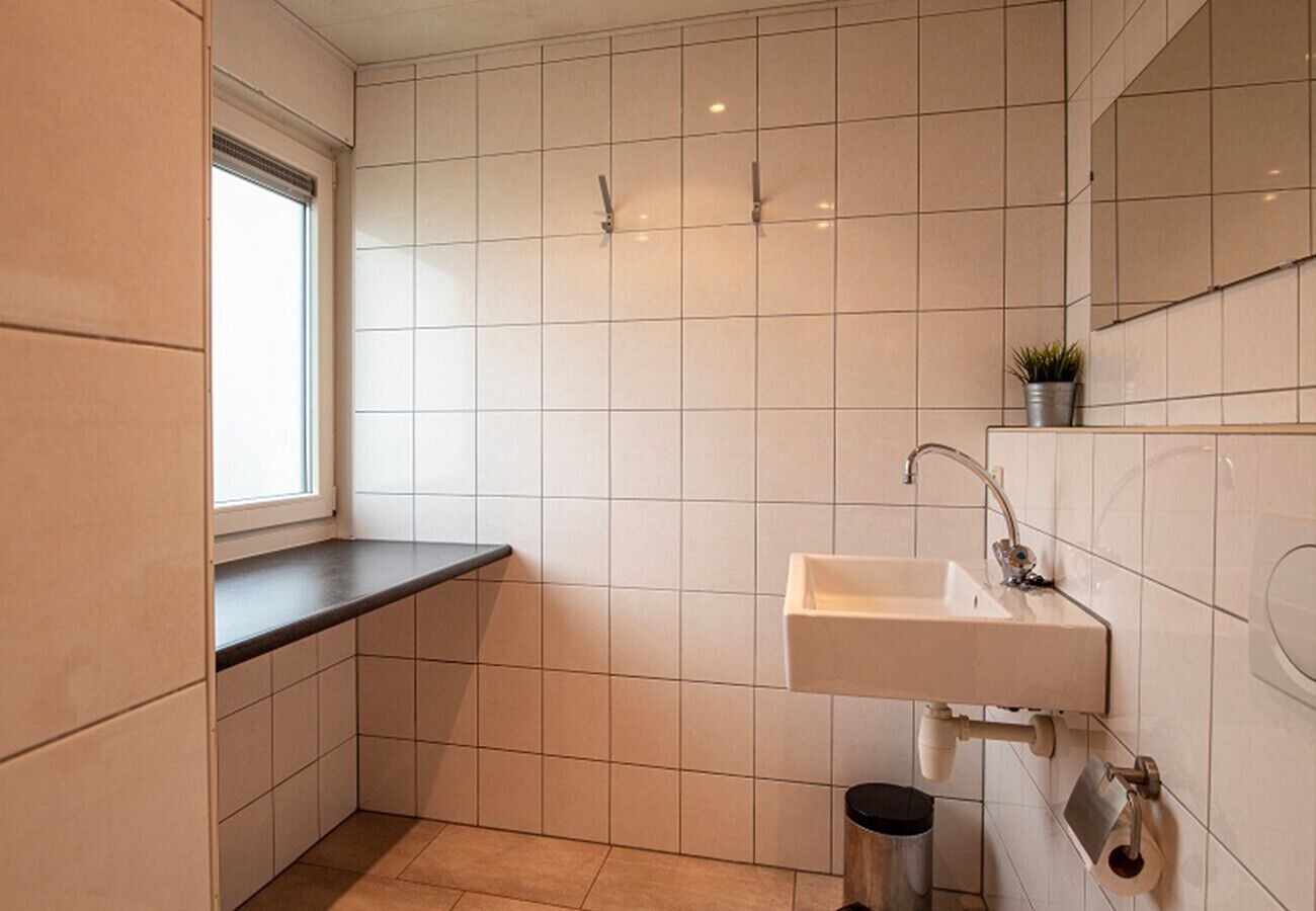 Une petite salle de bain moderne, avec des carreaux blancs, un lavabo, une fenêtre et une petite poubelle.