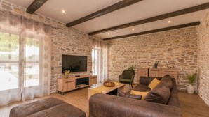 Un salon avec des murs en pierre, un meuble de rangement en bois pour l’équipement audiovisuel, un canapé en cuir marron et un téléviseur.