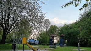 A playground with a yellow slide and climbing structures, surrounded by trees and a blue building in the background. - Bungalowpark Simpelveld - Castra 47 (Simpelveld)