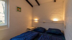 A small, single-bed room with a white brick wall, a window, and a nightstand. - Bungalowpark Simpelveld - Castra 47 (Simpelveld)