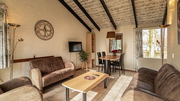 A living room with a sofa, coffee table, TV, and a dining area with chairs and a table. - Bungalowpark Simpelveld - Castra 40 (Simpelveld)