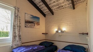 A room with two single beds, a window with curtains, a wall-mounted light fixture, and a picture on the wall. - Bungalowpark Simpelveld - Castra 40 (Simpelveld)