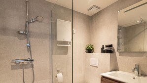 Une salle de bain moderne avec une douche à parois de verre, un lavabo avec un miroir et une plante en pot posée sur le meuble-lavabo.