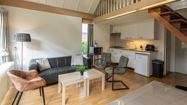 Un salon moderne avec un canapé, des fauteuils, une table basse et une cuisine en arrière-plan.