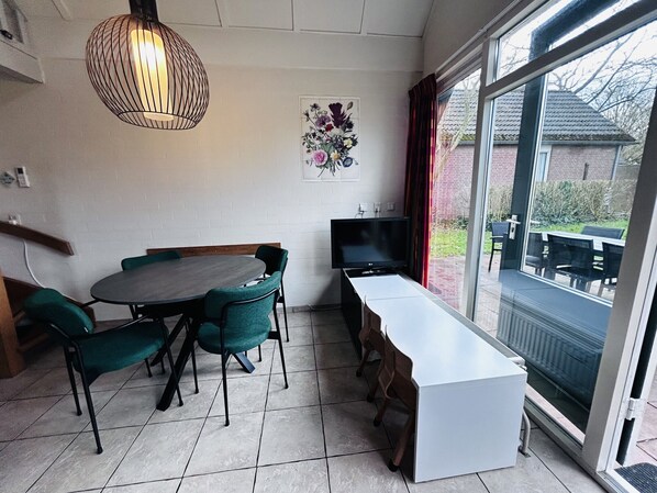 A dining area with a round table and chairs, a television, and a large window with a view of the outside.