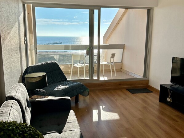 A modern living room with a large sliding glass door leading to a balcony with a view of the sea. - Cozy studio with sea view, pets allowed (Saint-Jean-de-Monts)