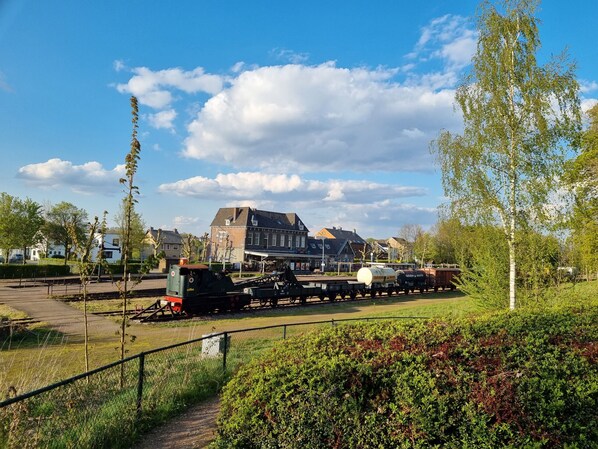 A train station with a building in the background, surrounded by greenery and a clear sky.