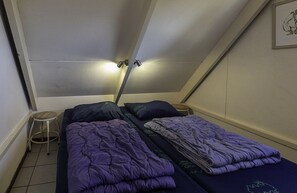 A small, triangular room with two beds, a stool, and a ceiling light. - Bungalowpark Simpelveld - Alpha 64 (Simpelveld)