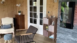 Une pièce aux murs en bois, avec une porte blanche, une chaise noire, un petit tabouret, une bibliothèque et une cheminée.