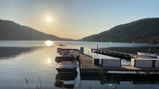 Un lac paisible où des bateaux sont amarrés à un quai en bois, le tout entouré de collines.