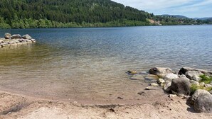 Un lac aux eaux limpides, bordé d’une rive rocheuse, avec une colline boisée en arrière-plan.