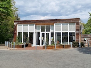 A modern building with large windows, a wooden facade, and a paved entrance area with bollards.