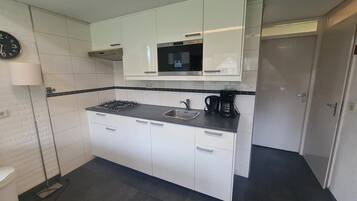 Una cucina compatta con mobili bianchi, un fornello a gas, un lavello e una macchina per il caffè.