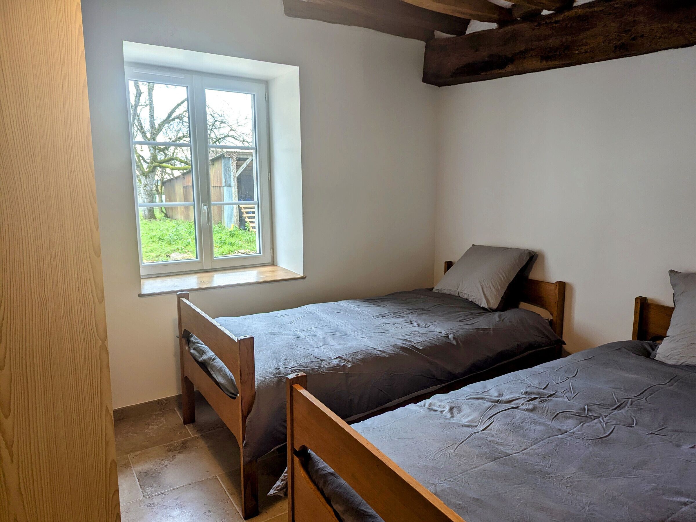 A bedroom with two wooden beds, a window with a view of a garden, and a sloped ceiling.