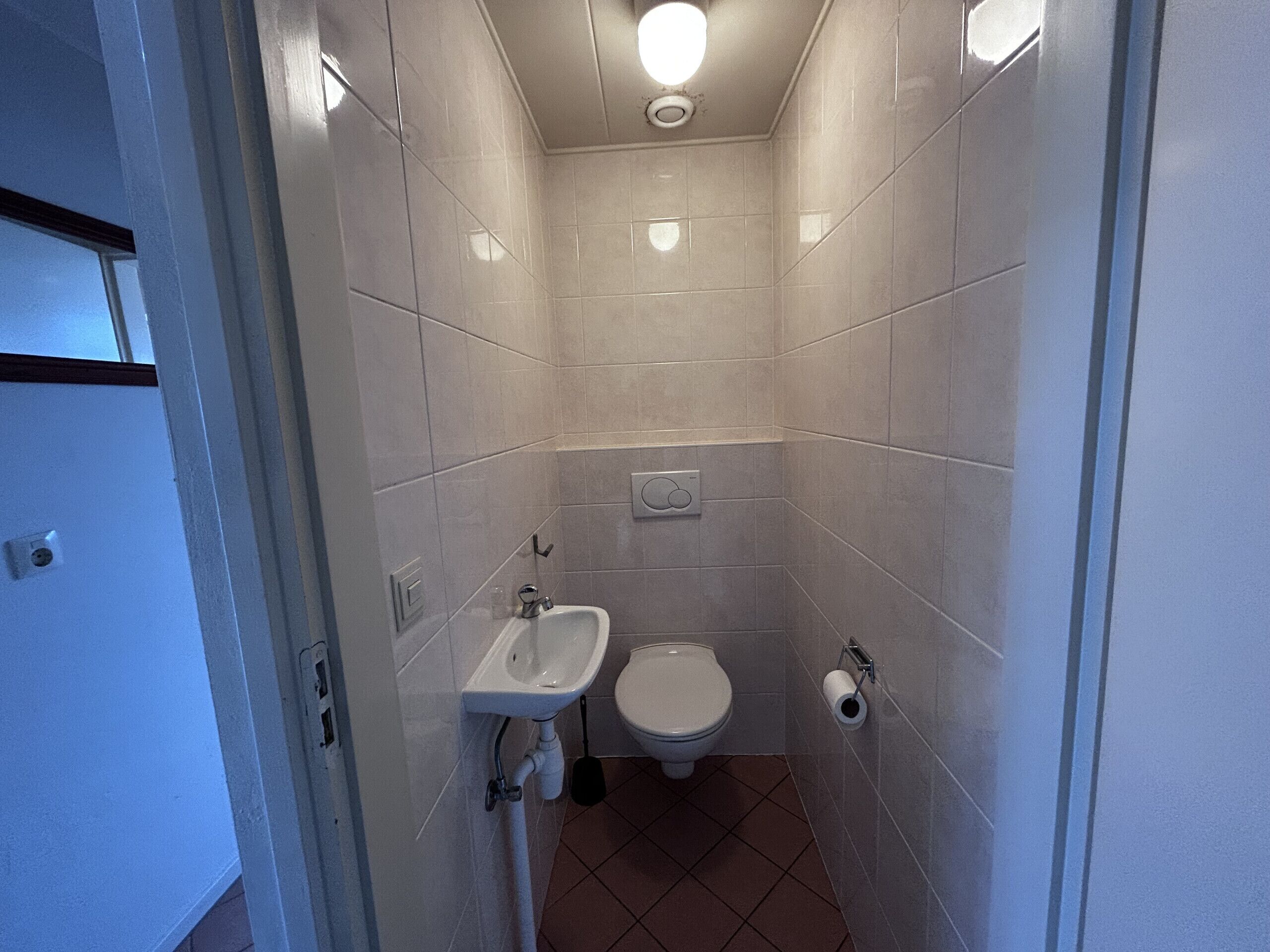 Et lille badeværelse med toilet, håndvask og toiletpapirholder.