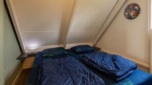 Una habitación pequeña y funcional con dos camas, una ventana con cortina y un reloj en la pared.