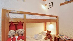 Ein Stockbett mit einem Teddybären auf der unteren Liege, ein kleiner Tisch mit einer Zeitschrift und ein gerahmtes Bild an der Wand.