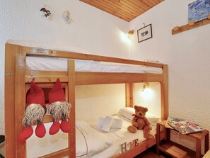 Ein Stockbett mit einem Teddybären auf der unteren Liege, ein kleiner Tisch mit einer Zeitschrift und ein gerahmtes Bild an der Wand.