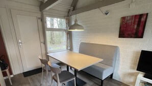 A compact room with a table and two chairs, a sofa, a television on a stand, and a window with curtains. - Bungalowpark Simpelveld - Alpha 77 (Simpelveld)