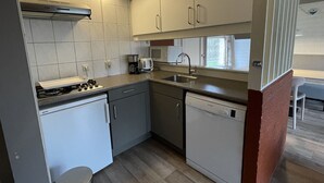 A compact kitchen with white cabinets, a gas stove, a dishwasher, and a window providing natural light. - Bungalowpark Simpelveld - Alpha 77 (Simpelveld)