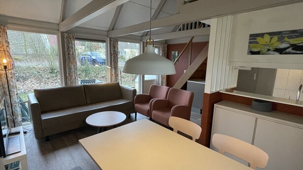 A modern interior with a sofa, chairs, a dining table, and a kitchen area. - Bungalowpark Simpelveld - Alpha 77 (Simpelveld)