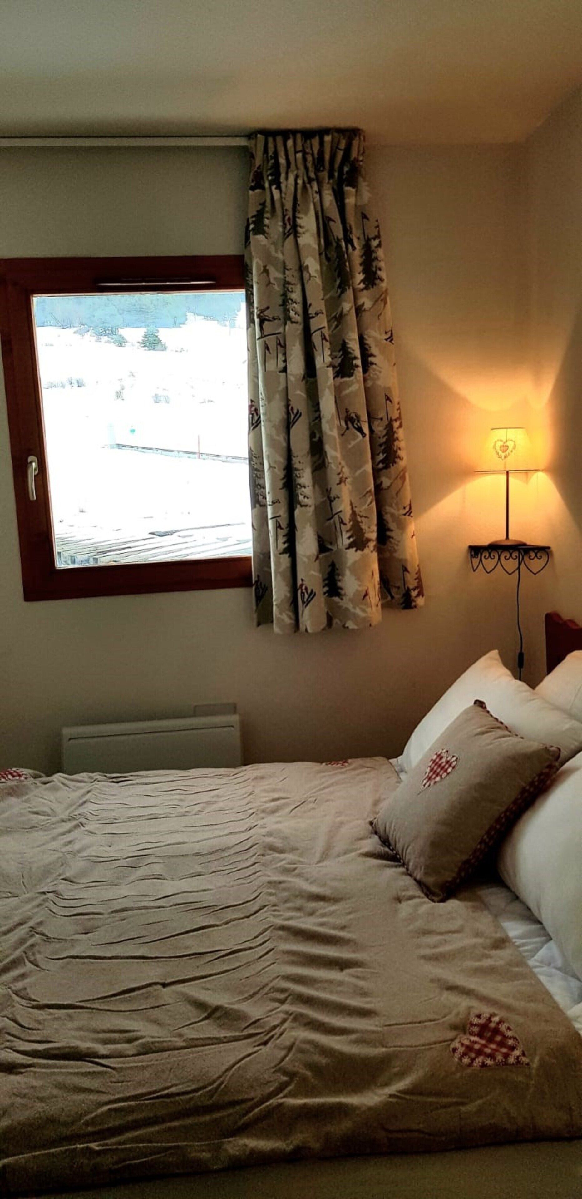 Una camera da letto con un letto, una finestra con tende, una lampada a parete e un termosifone.