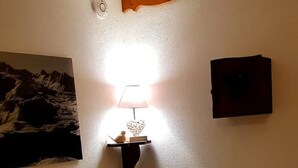A bedroom with a bed, a nightstand with a lamp, a wall-mounted shelf, and a framed picture. - Balcons B 011 - Parc Nat. Vanoise Appart. 6 Pers (Val-Cenis)