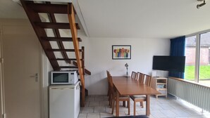 A dining area with a wooden table and chairs, a microwave, a TV, and a painting on the wall. - Bungalowpark Simpelveld - Delta 109 (Simpelveld)