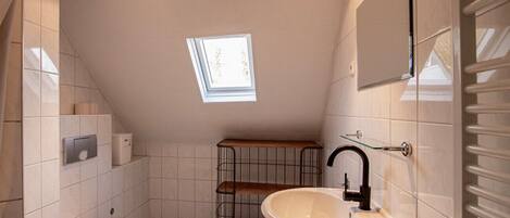 A small, modern bathroom with a skylight, a toilet, a sink, and a metal shelf unit.