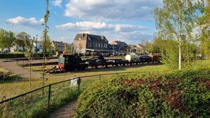Een treinstation met een gebouw op de achtergrond, omringd door groen en een heldere lucht.