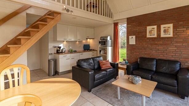 A modern interior with a kitchen, two black leather sofas, a wooden dining table, and a staircase. - Bungalowpark Simpelveld - Delta 148 (Simpelveld)