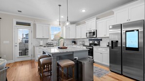 A modern kitchen with white cabinetry, stainless steel appliances, a central island with stools, and a view through the window. - Charming 4-bedroom house with WiFi, AC in wonderful North Augusta (North Augusta)