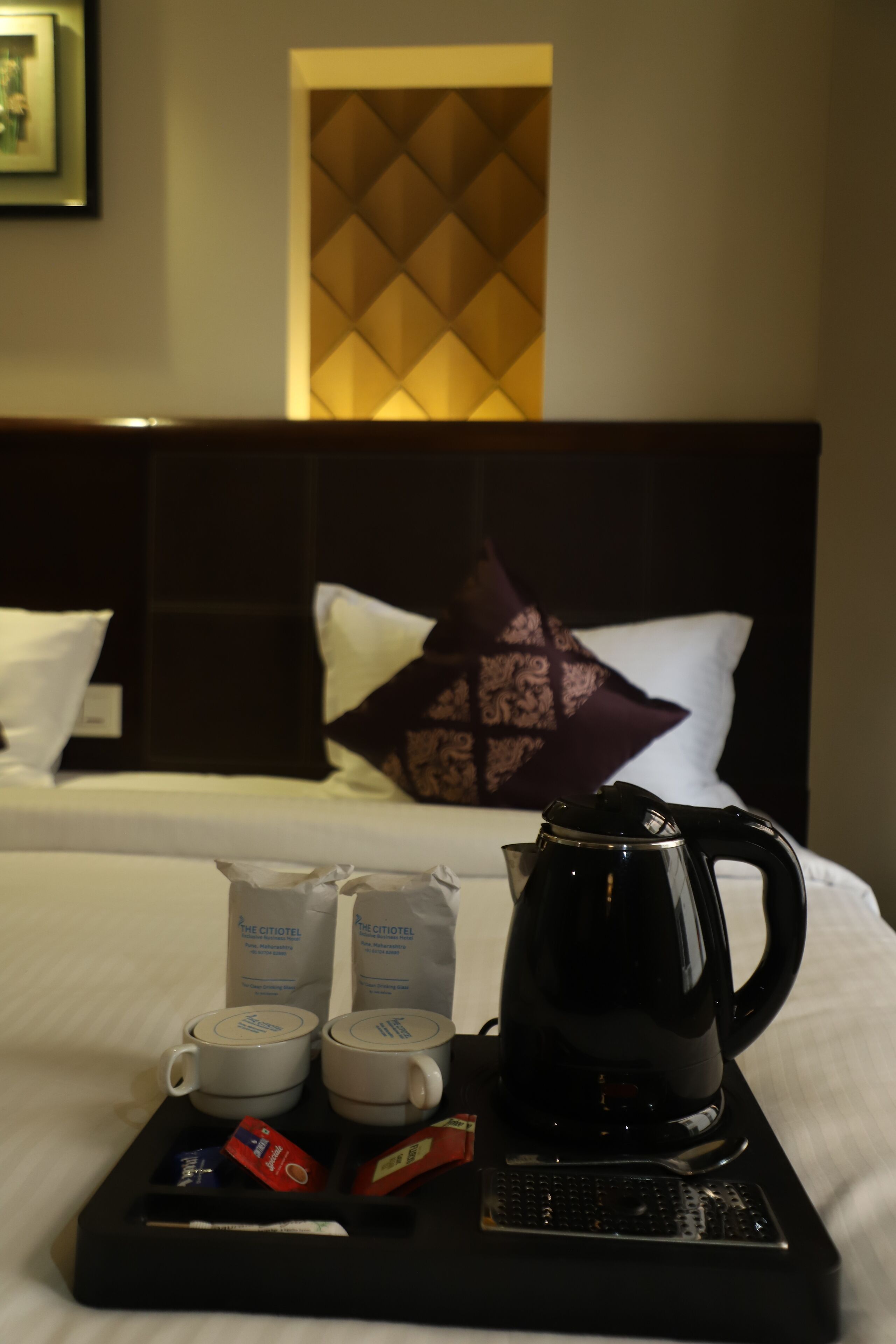 A hotel room with a neatly made bed, a tray with coffee-making equipment, and a pillow with a geometric pattern.