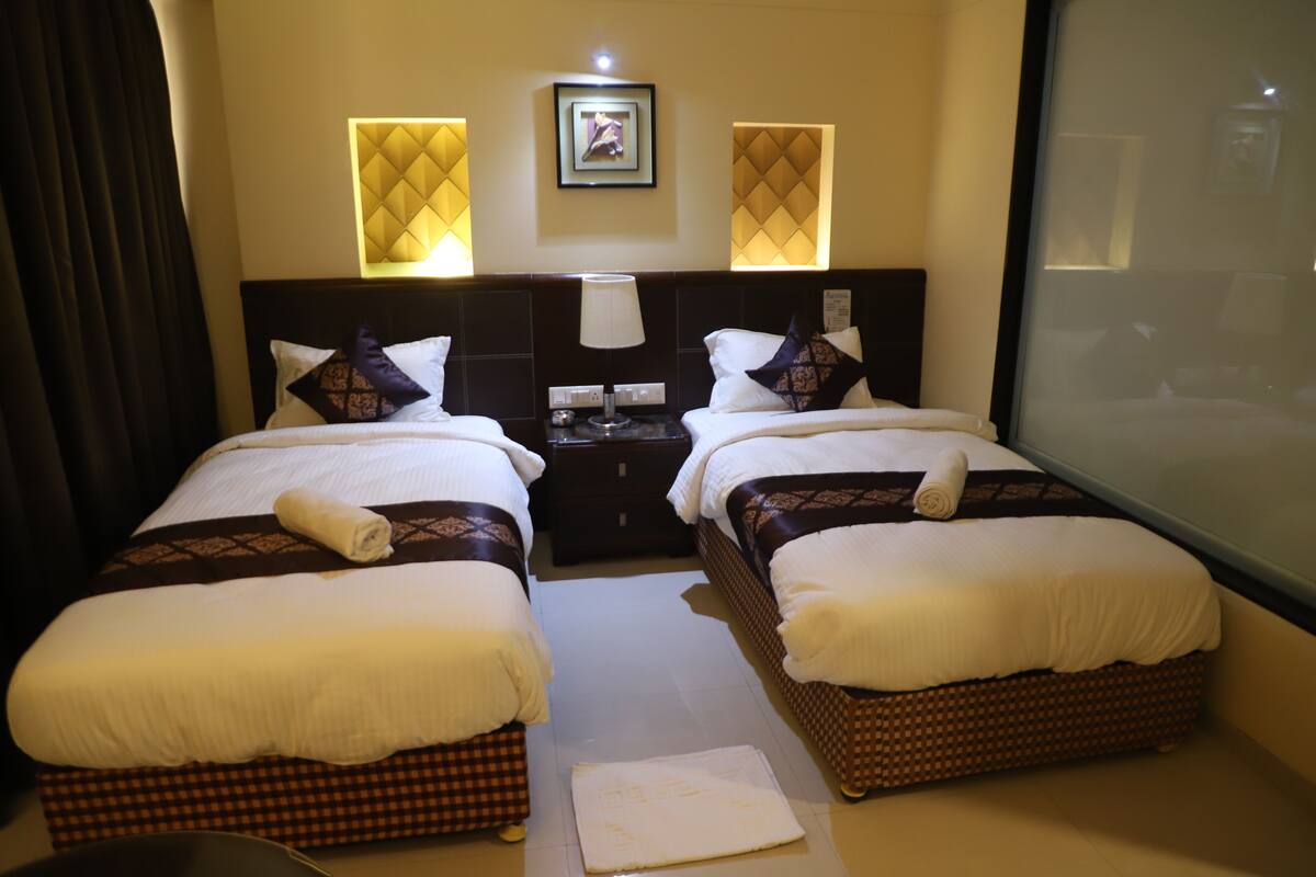 A hotel room with two beds, a nightstand, a lamp, and a framed picture on the wall.