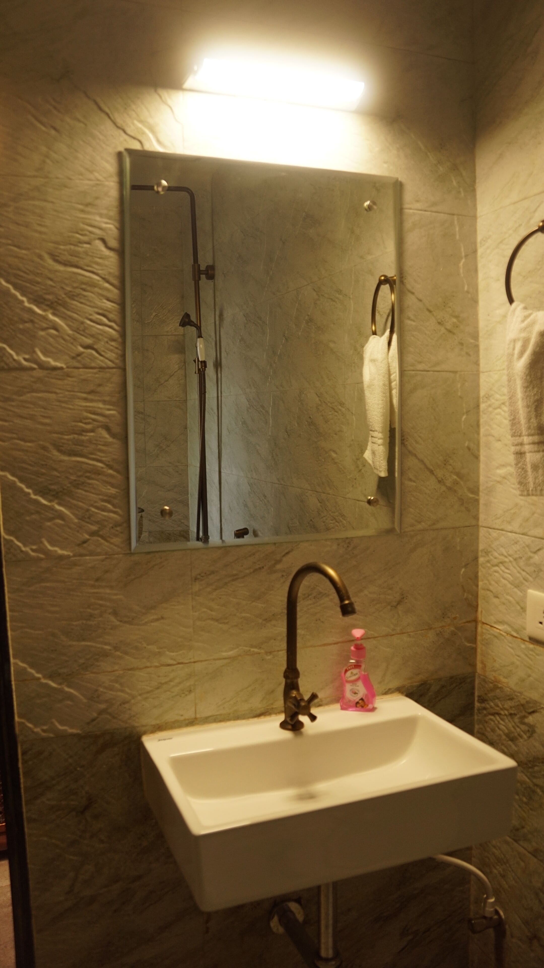 Une salle de bain avec un lavabo blanc, un miroir, un porte-serviettes et une douche.