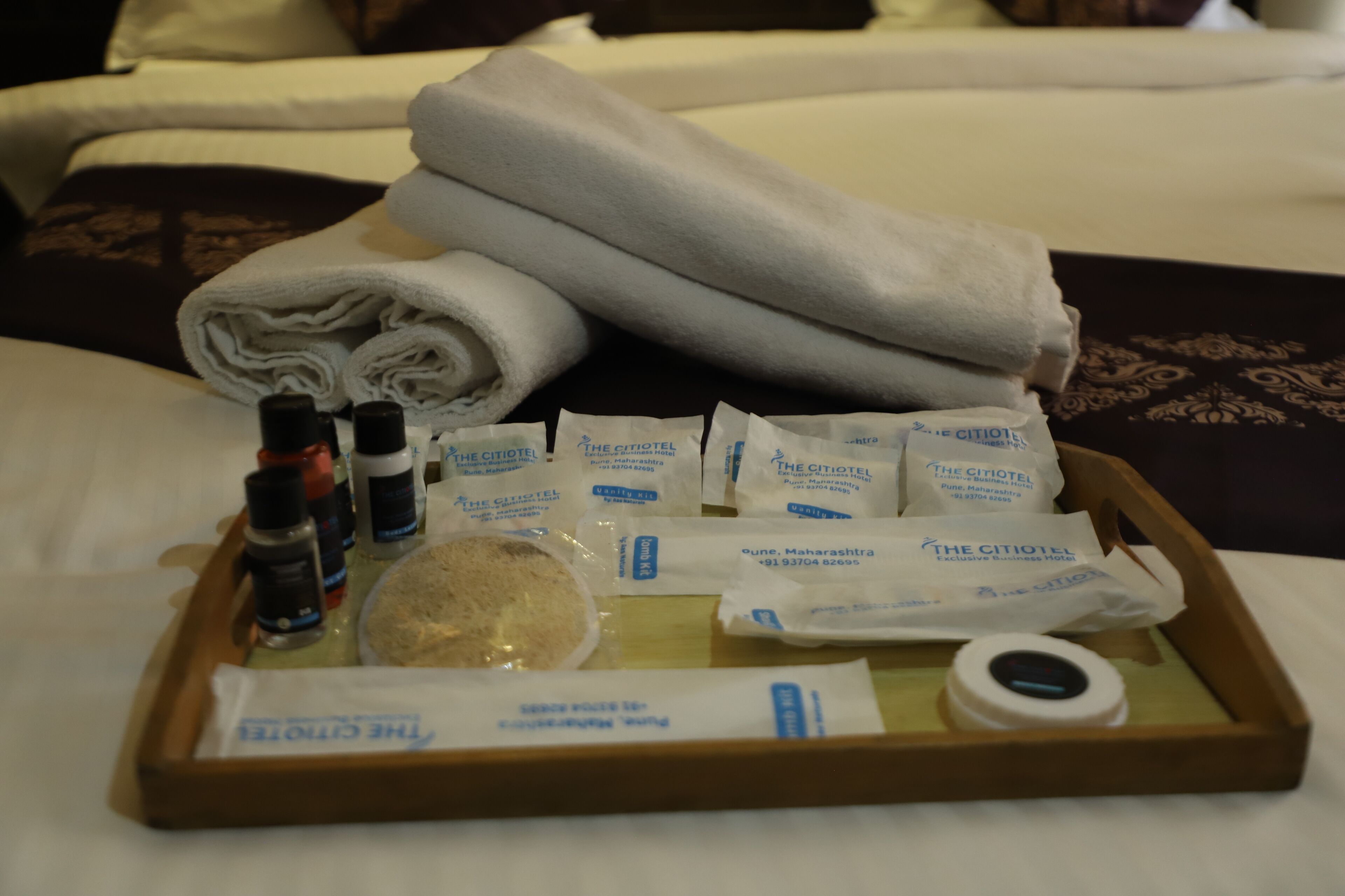 A tray with toiletries, including bottles, a bar of soap, and towels, on a bed.