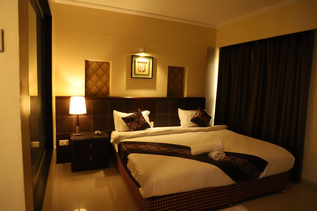 A hotel room with a large bed, a nightstand, a lamp, and a framed picture on the wall.