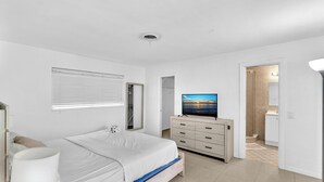 A bedroom with a bed, a TV, a wardrobe, and a bathroom visible through an open door.