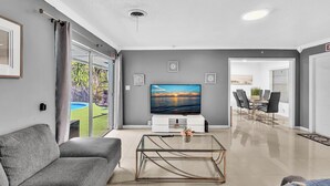 A modern living room with a flat-screen TV, grey sofa, and a glass coffee table.
