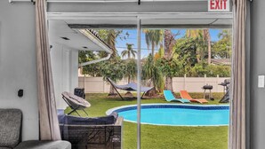 A room with a sliding glass door leading to a backyard with a swimming pool, outdoor furniture, and a hammock.
