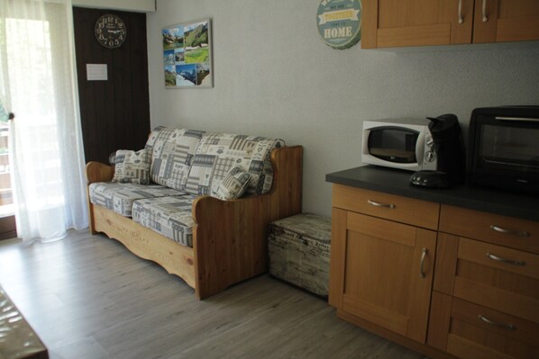 A cozy room with a wooden sofa, a small cabinet, a microwave, and a television.