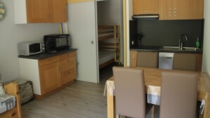 Een kleine keuken met houten kastjes, een magnetron, een spoelbak en een eettafel met stoelen.