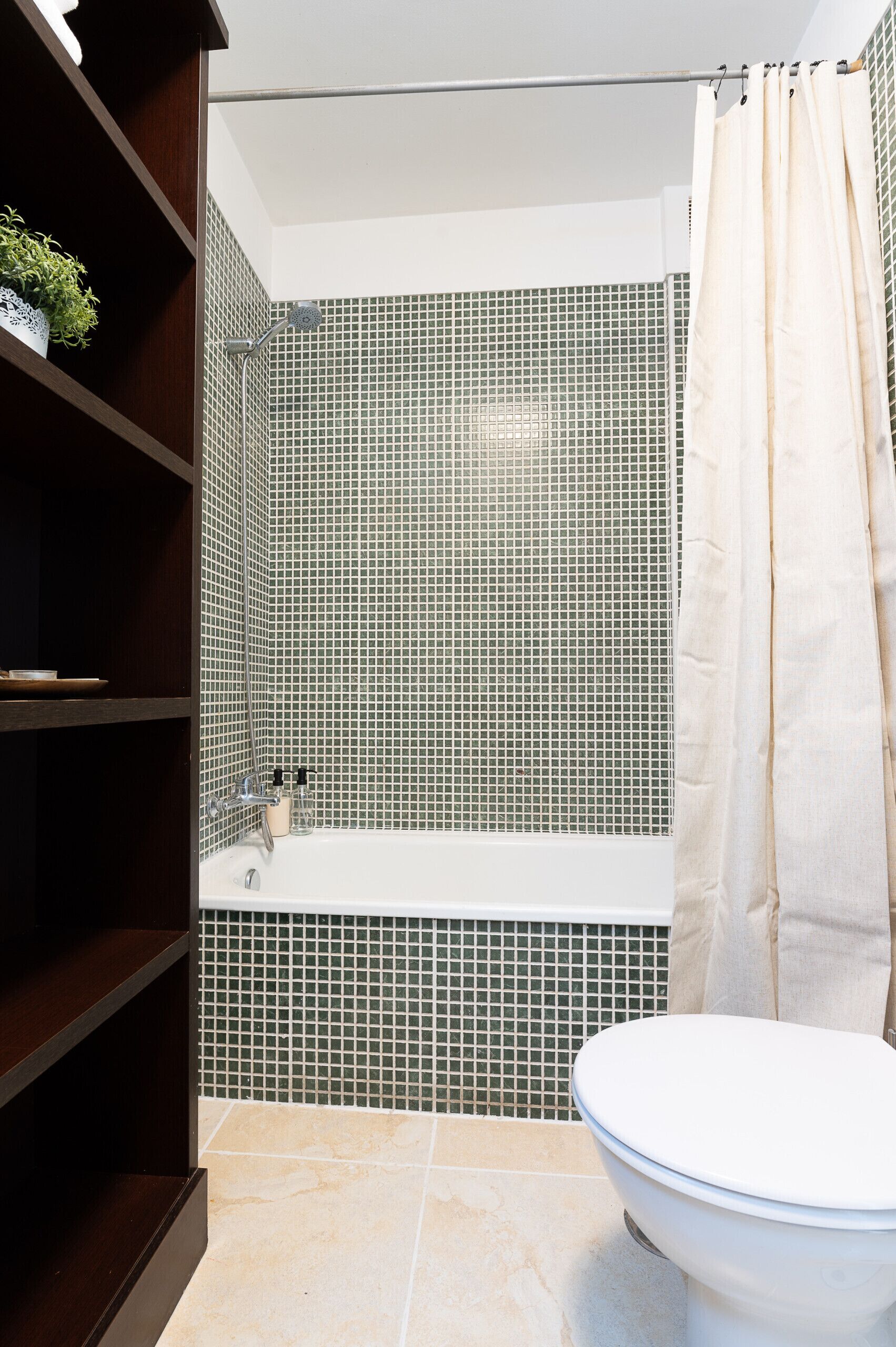 Un baño con bañera, inodoro y repisas con artículos de aseo.
