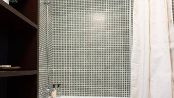 Un baño con bañera, inodoro y repisas con artículos de aseo.