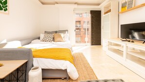 Un dormitorio moderno con cama, sofá, televisión y vistas al balcón.