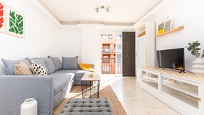 Una sala de estar moderna con un sofá gris, un televisor sobre un mueble blanco y obras de arte en las paredes.
